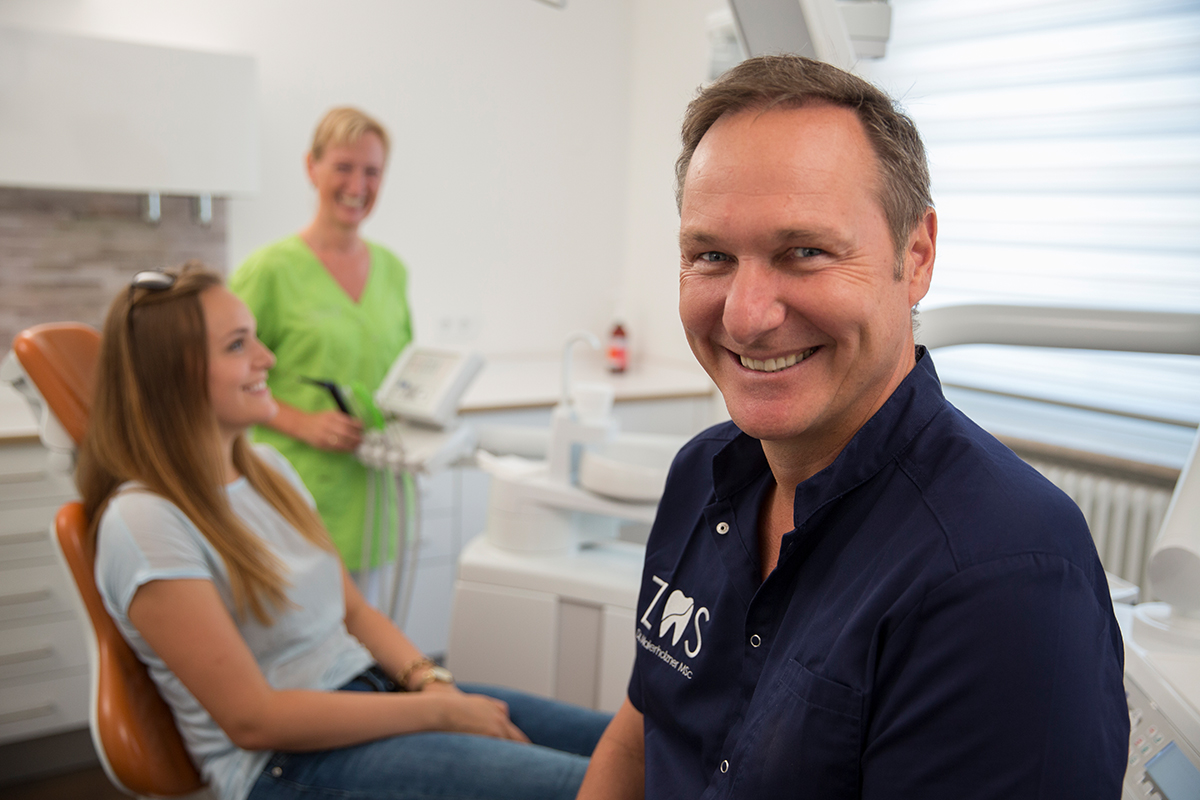 Zahnarzt sitzt im Behandlungsraum und blickt in die Kamera