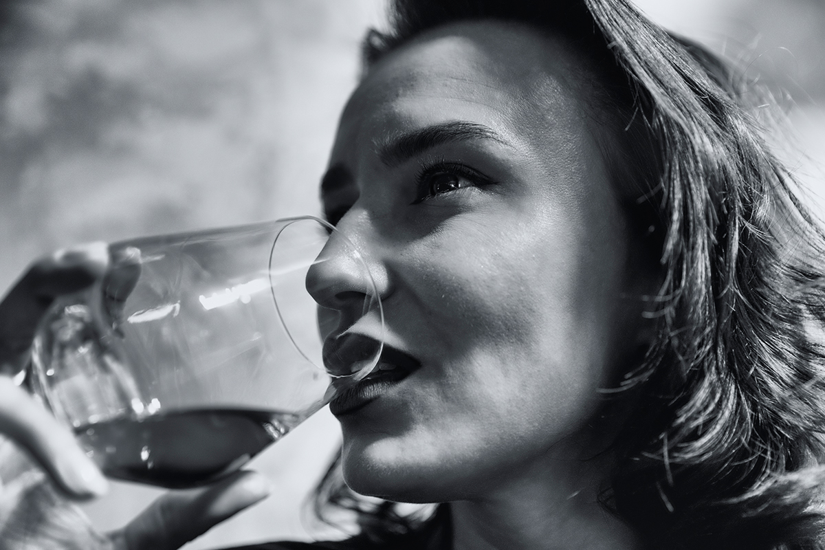 Frau hält sich ein Glas an den Mund und blickt in die Ferne
