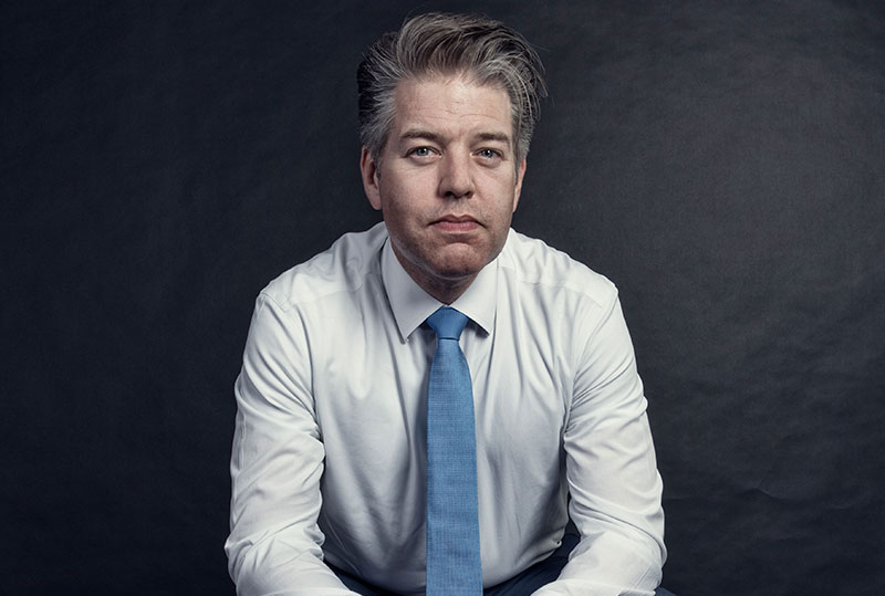 Herr mit Hemd und Krawatte lehnt mit seinen Ellenbogen auf den Beinen.