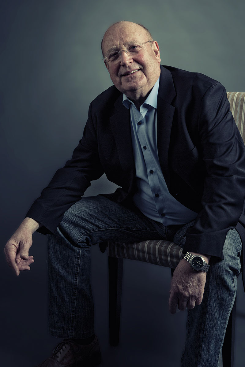 Herr sitzt auf Stuhl und lehnt mit den Armen auf seinen Knien.